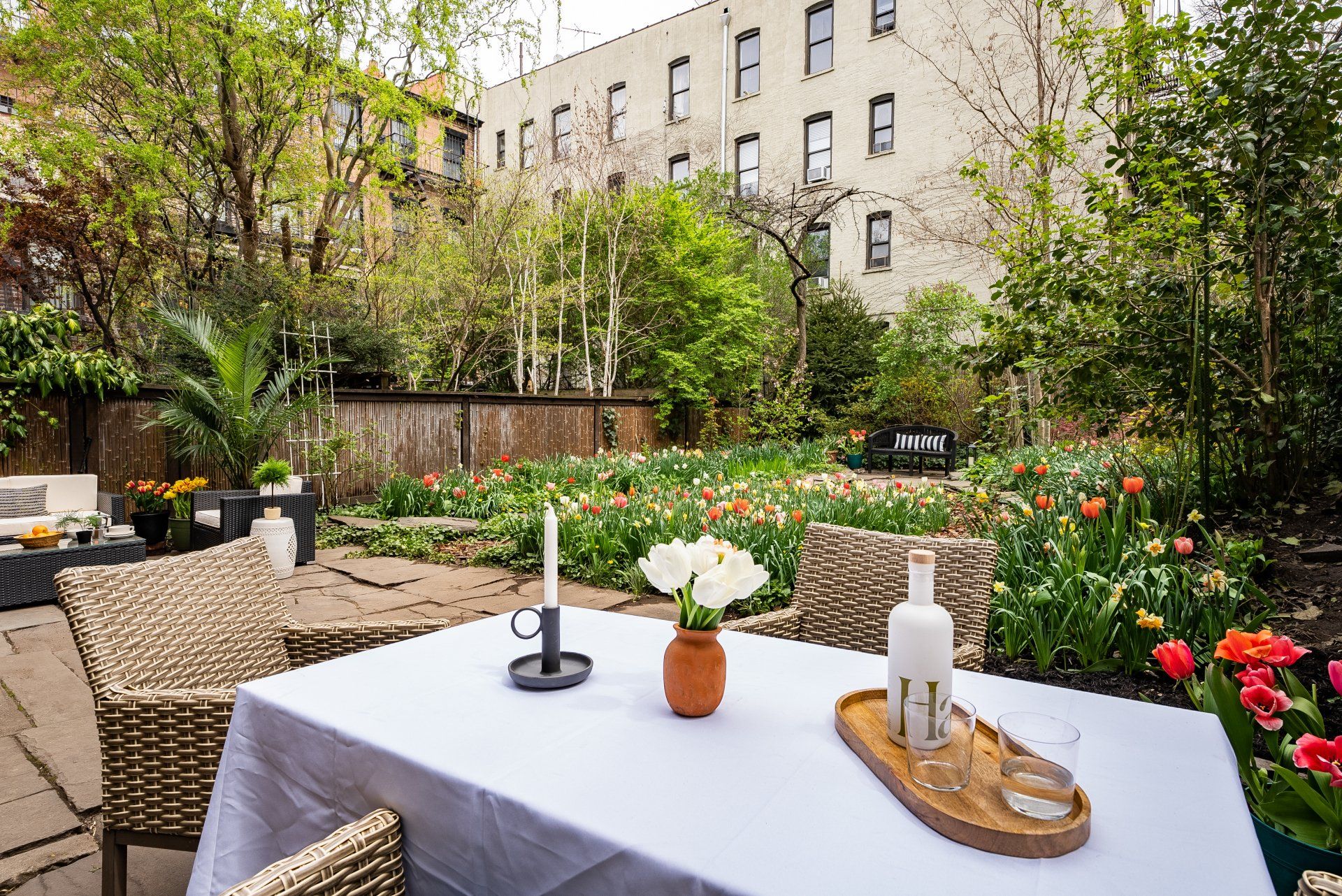 A table with a white tablecloth and a vase of flowers on it in a garden.