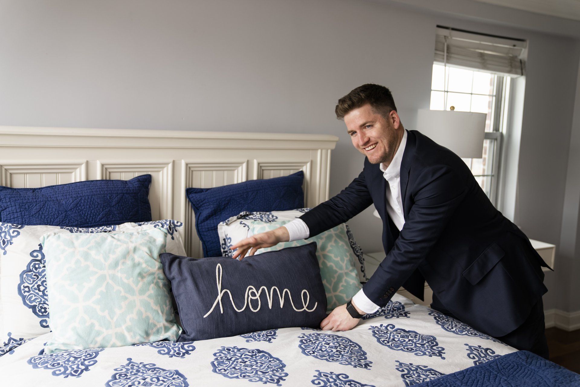 A man in a suit is arranging pillows on a bed.