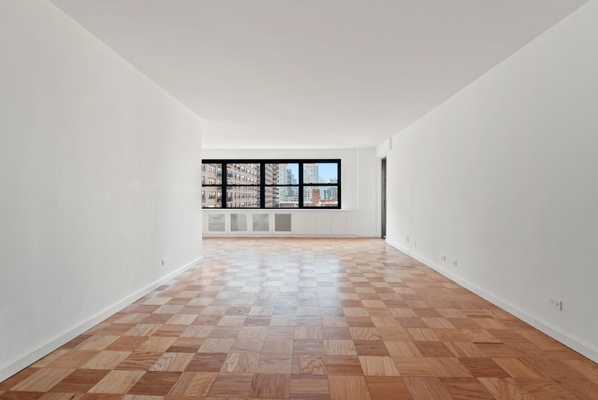 An empty living room with wooden floors and white walls.