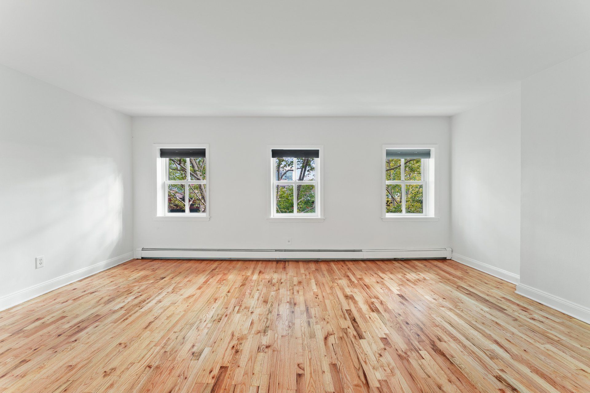 An empty room with hardwood floors and three windows.