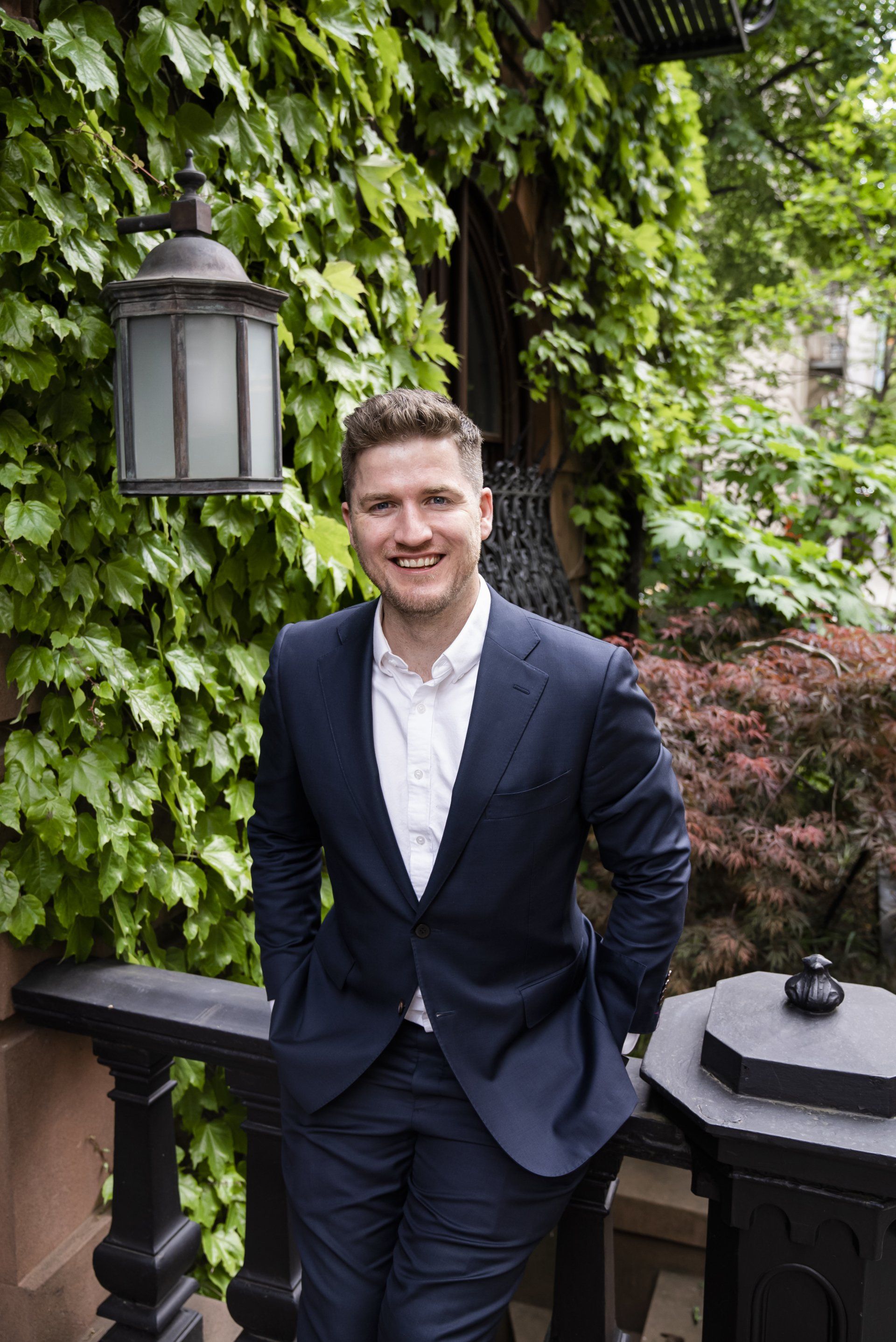 A man in a suit is standing on a balcony with his hands in his pockets.