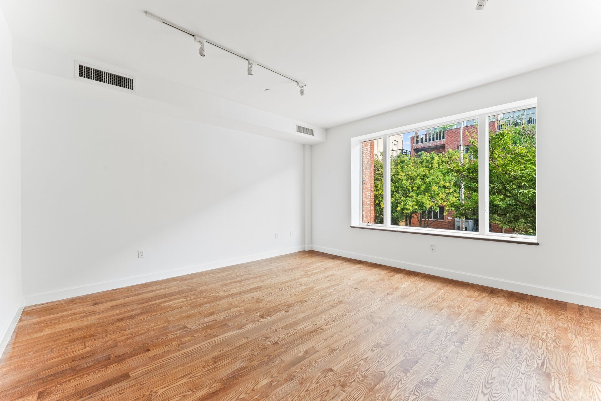 An empty living room with hardwood floors and a large window.