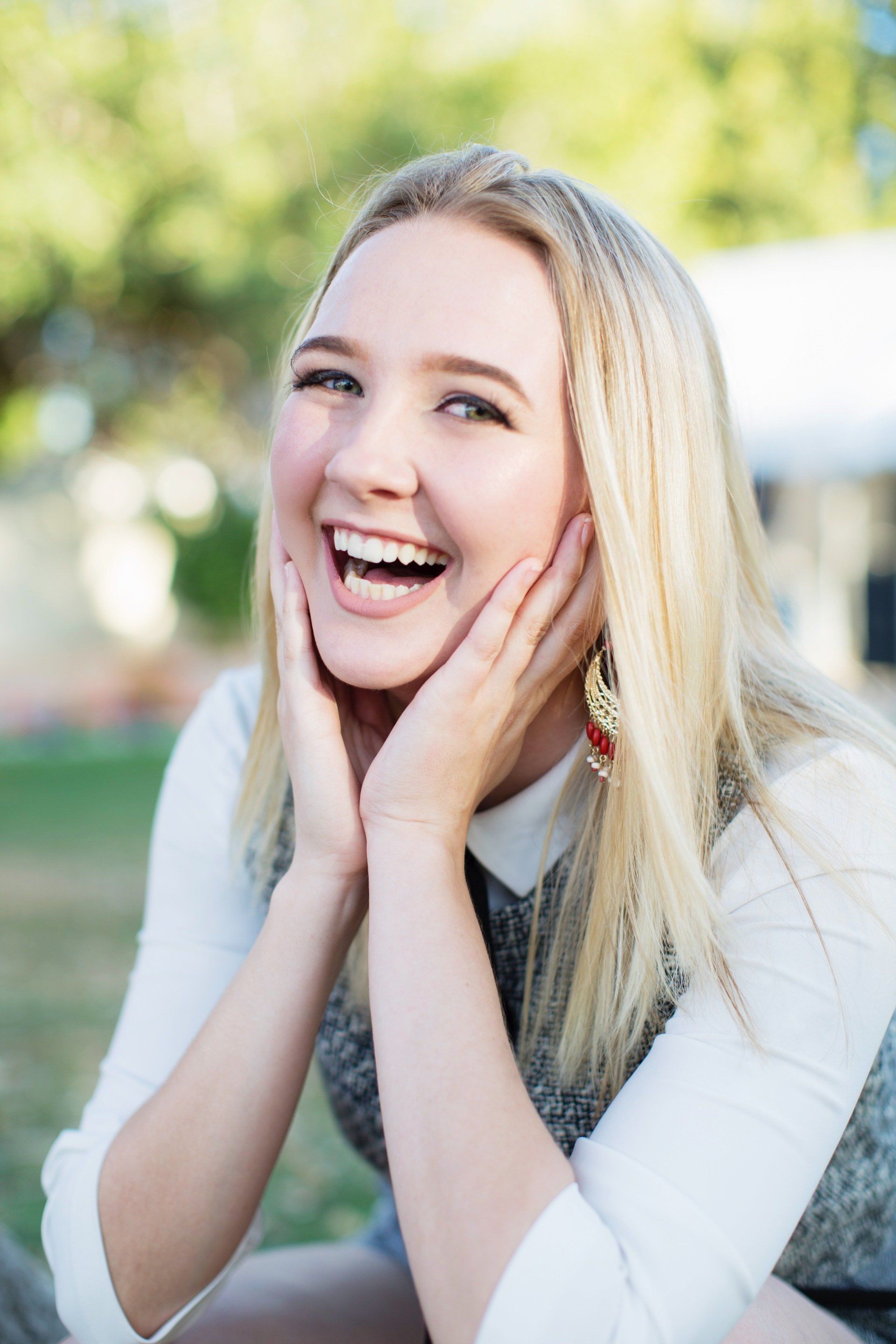 A young woman is smiling with her hands on her face.