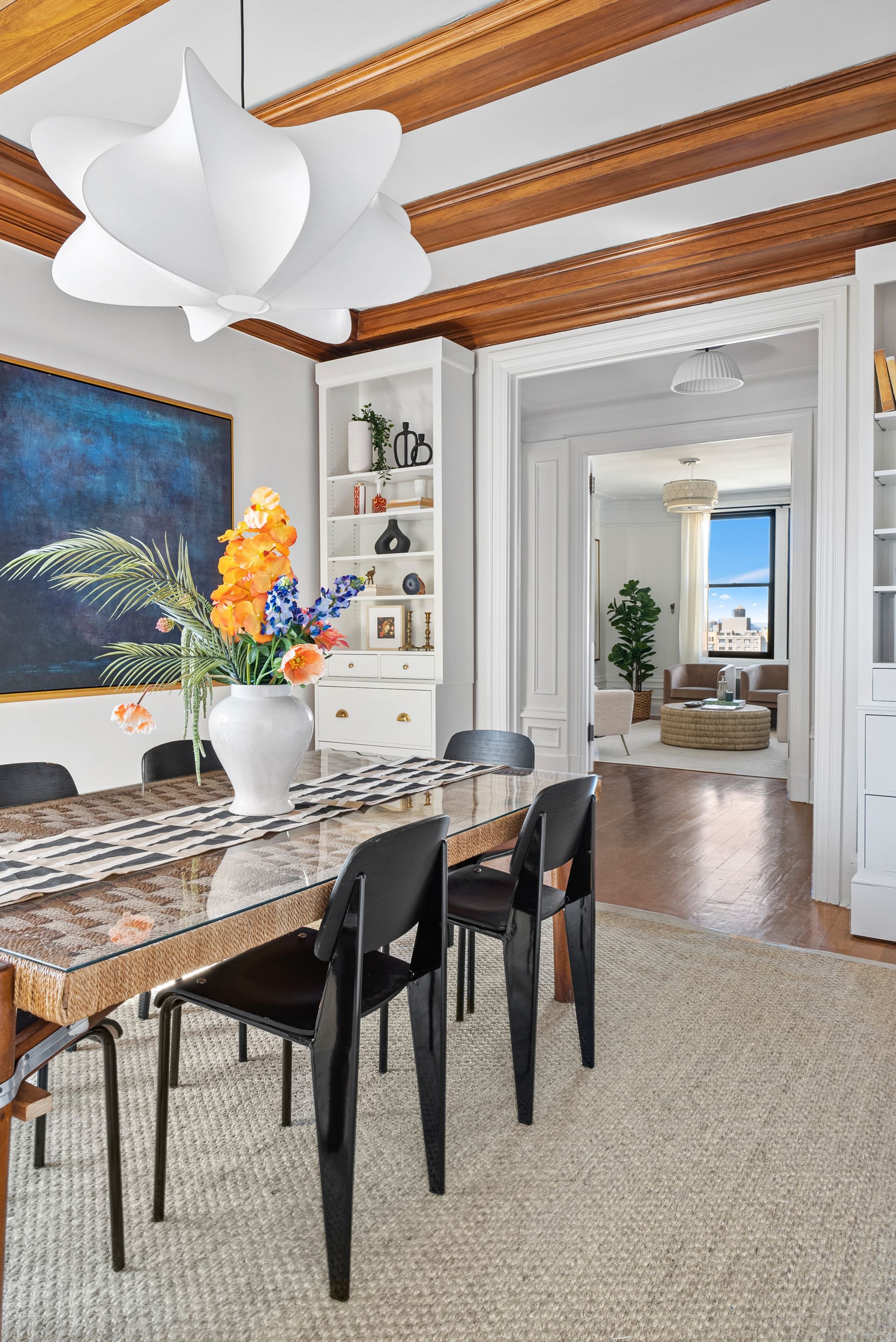A dining room with a table and chairs and a vase of flowers on the table.