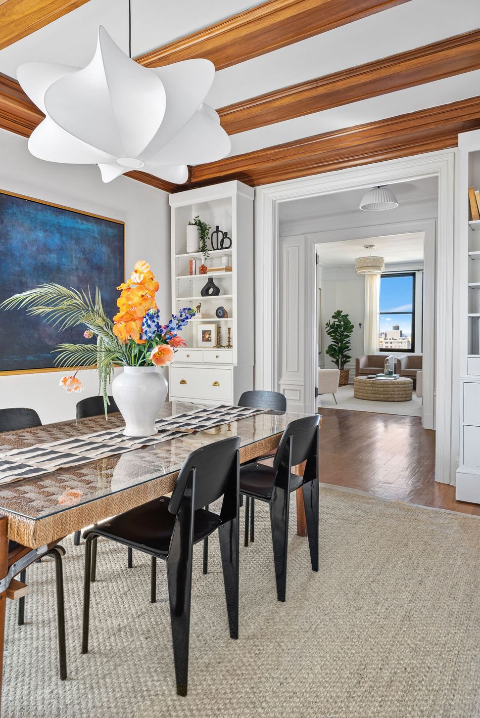 A dining room with a table and chairs and a vase of flowers on the table.