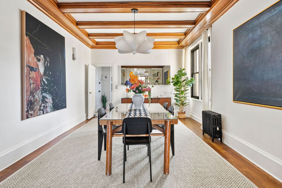 A dining room with a table and chairs and a painting on the wall.