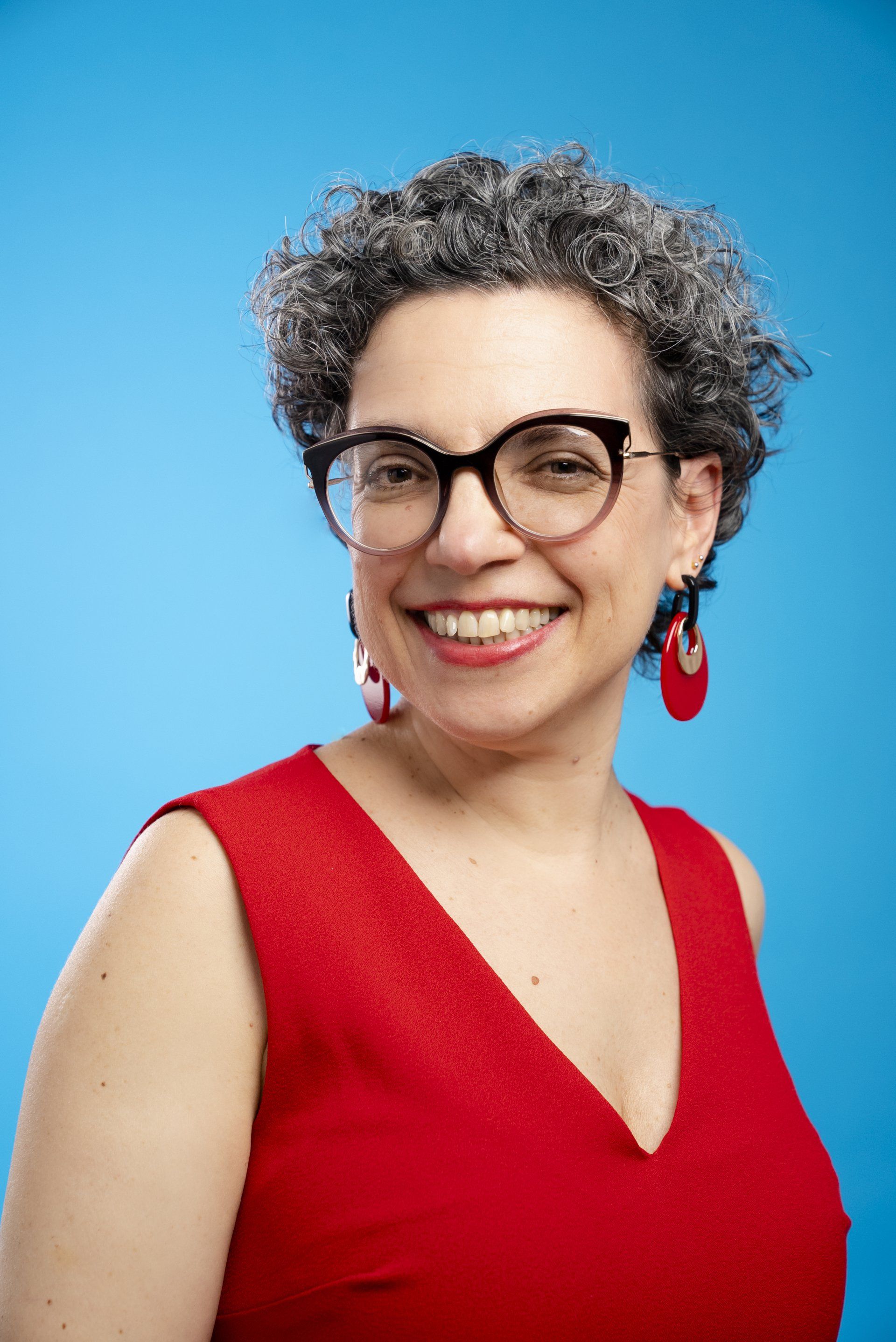 A woman wearing glasses and a red dress is smiling for the camera.
