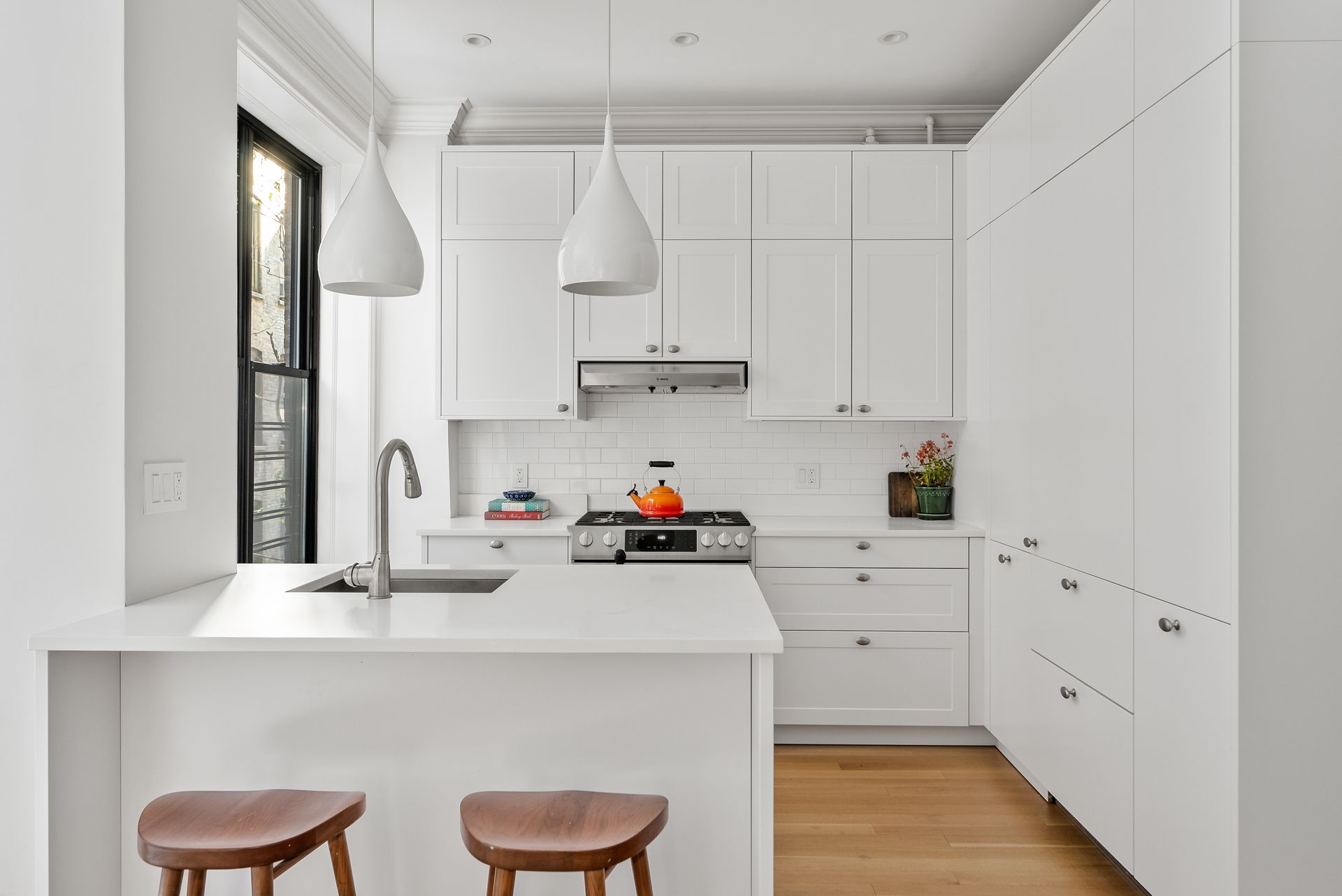 A kitchen with white cabinets , a stove , a sink , and two stools.