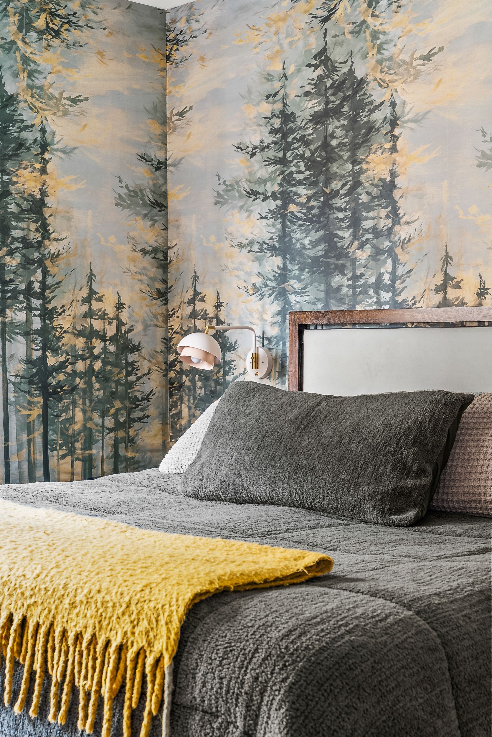 A bedroom with a bed and a painting of trees on the wall.