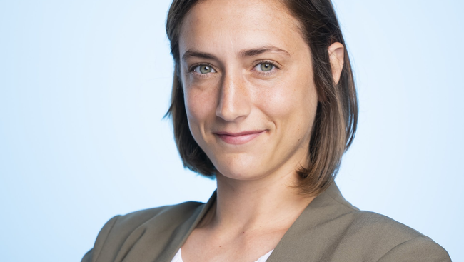 A woman in a suit is smiling and looking at the camera.