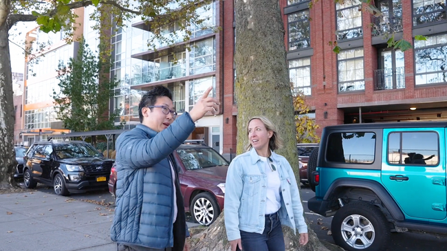 A man and a woman are standing next to a tree in front of a building.