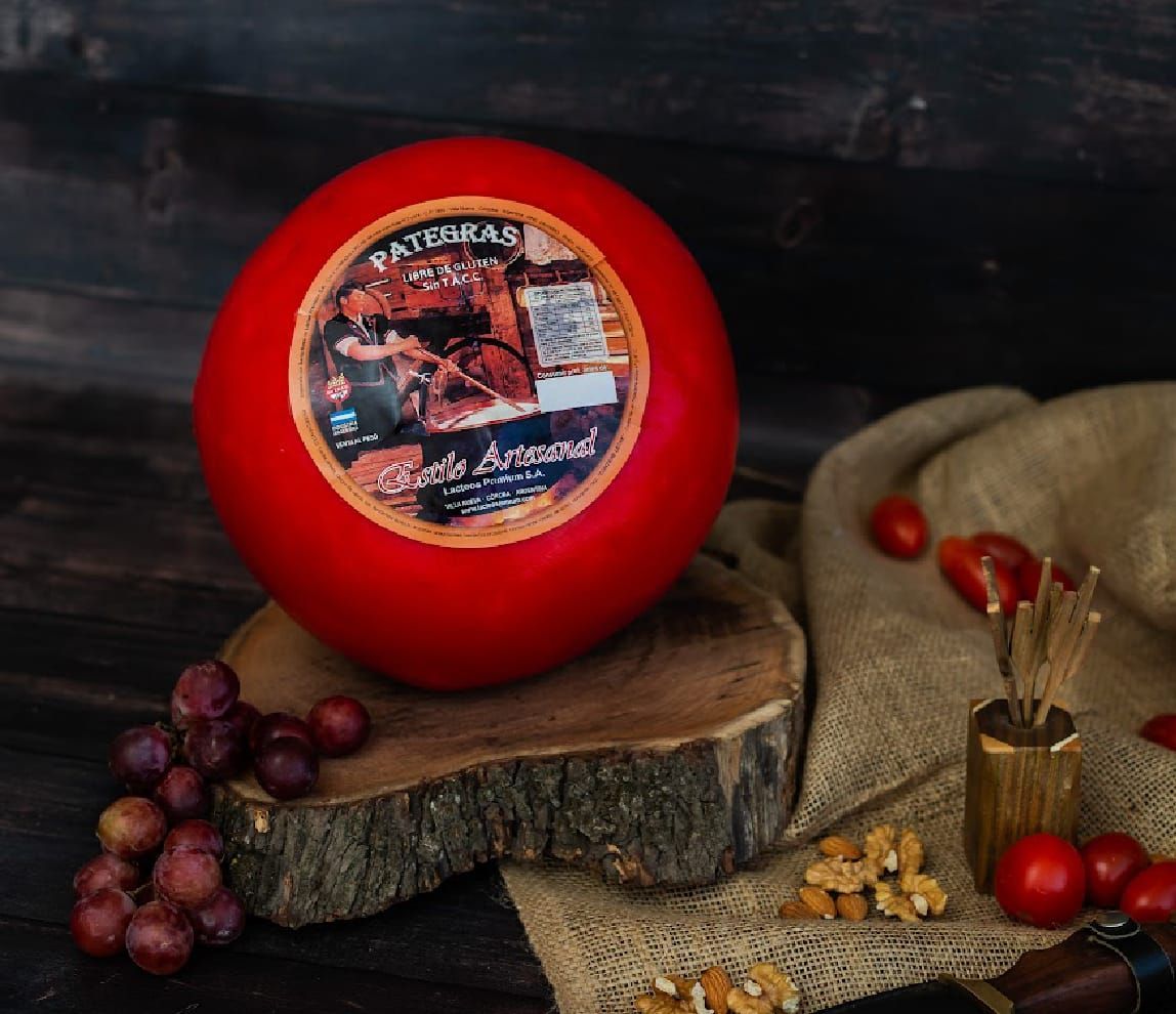 Rueda de queso rojo sobre base de madera con uvas, tomates y nueces.