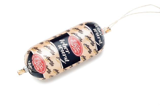Salchicha Leberwurst envuelta en plástico y con una cuerda encima, sobre fondo blanco.