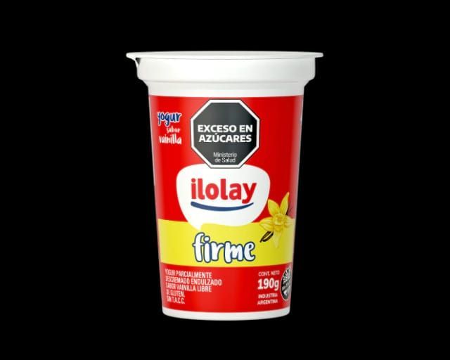 Vaso de yogur Ilolay, color rojo y blanco, etiquetado “Firme” sabor vainilla, con advertencia de “Exceso de Azúcares”.