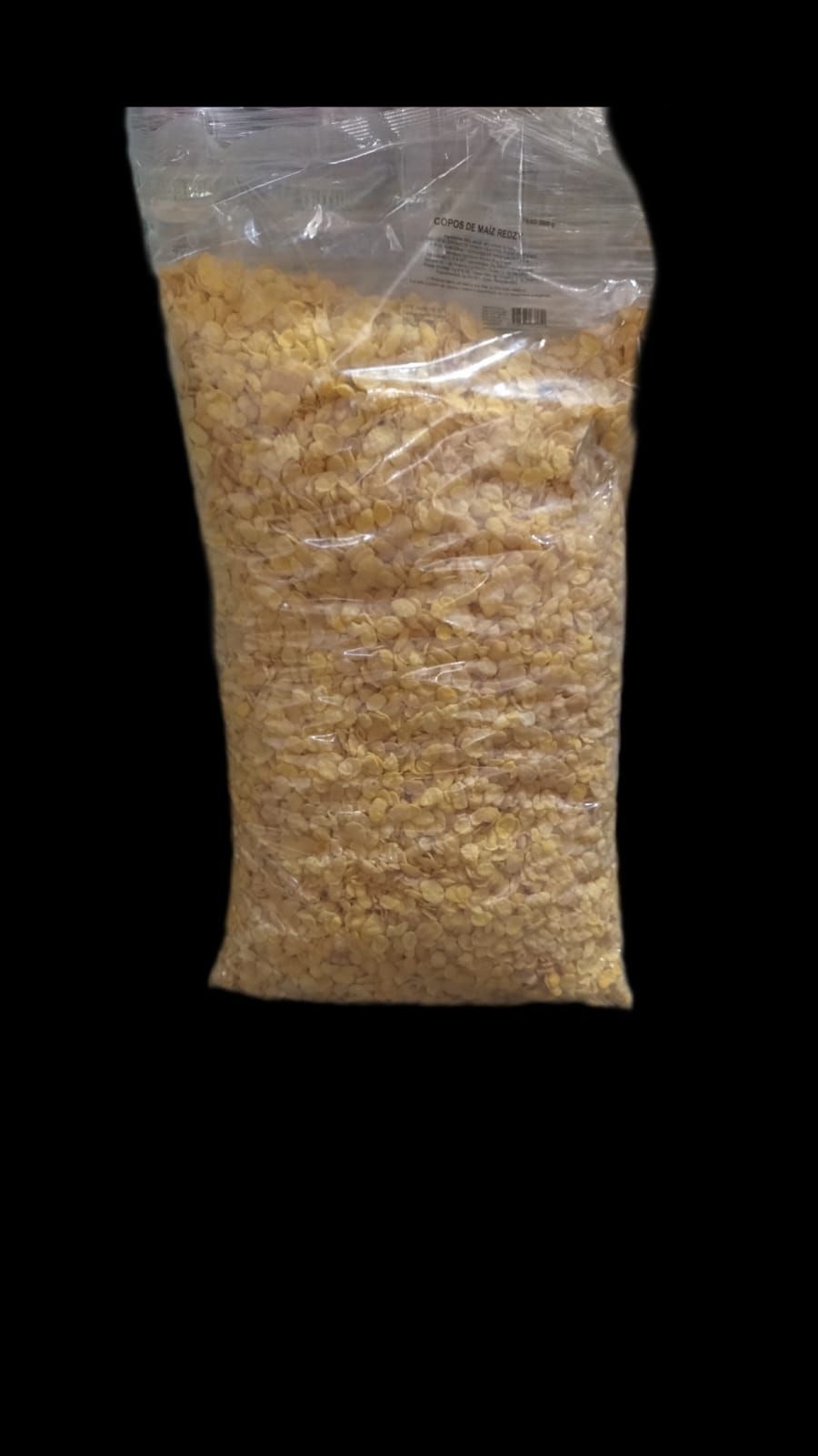 Bolsa de material de color canela, probablemente trozos pequeños, en una bolsa de plástico transparente sobre un fondo negro.
