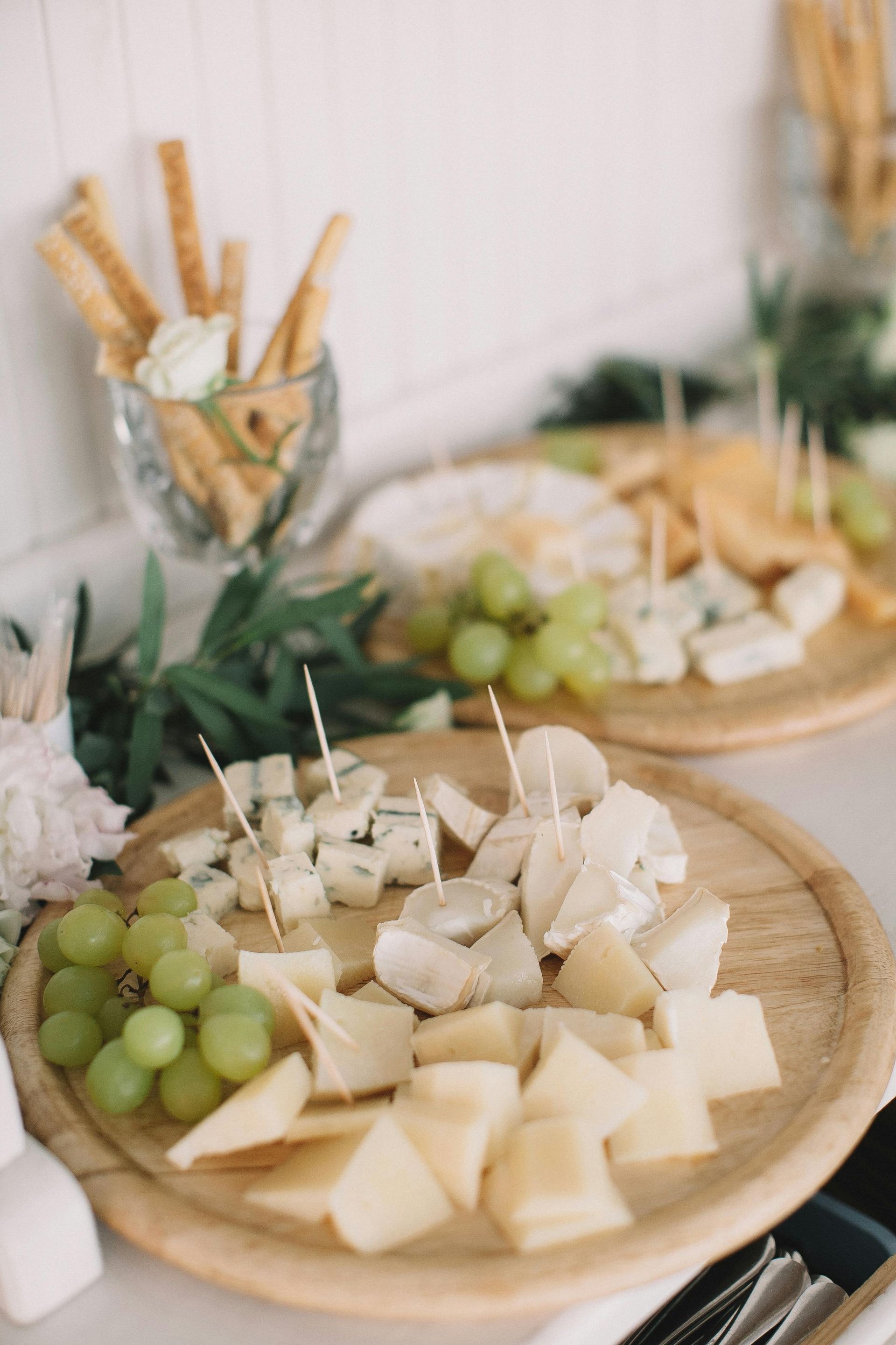Una tabla de cortar de madera cubierta con queso y uvas sobre una mesa.