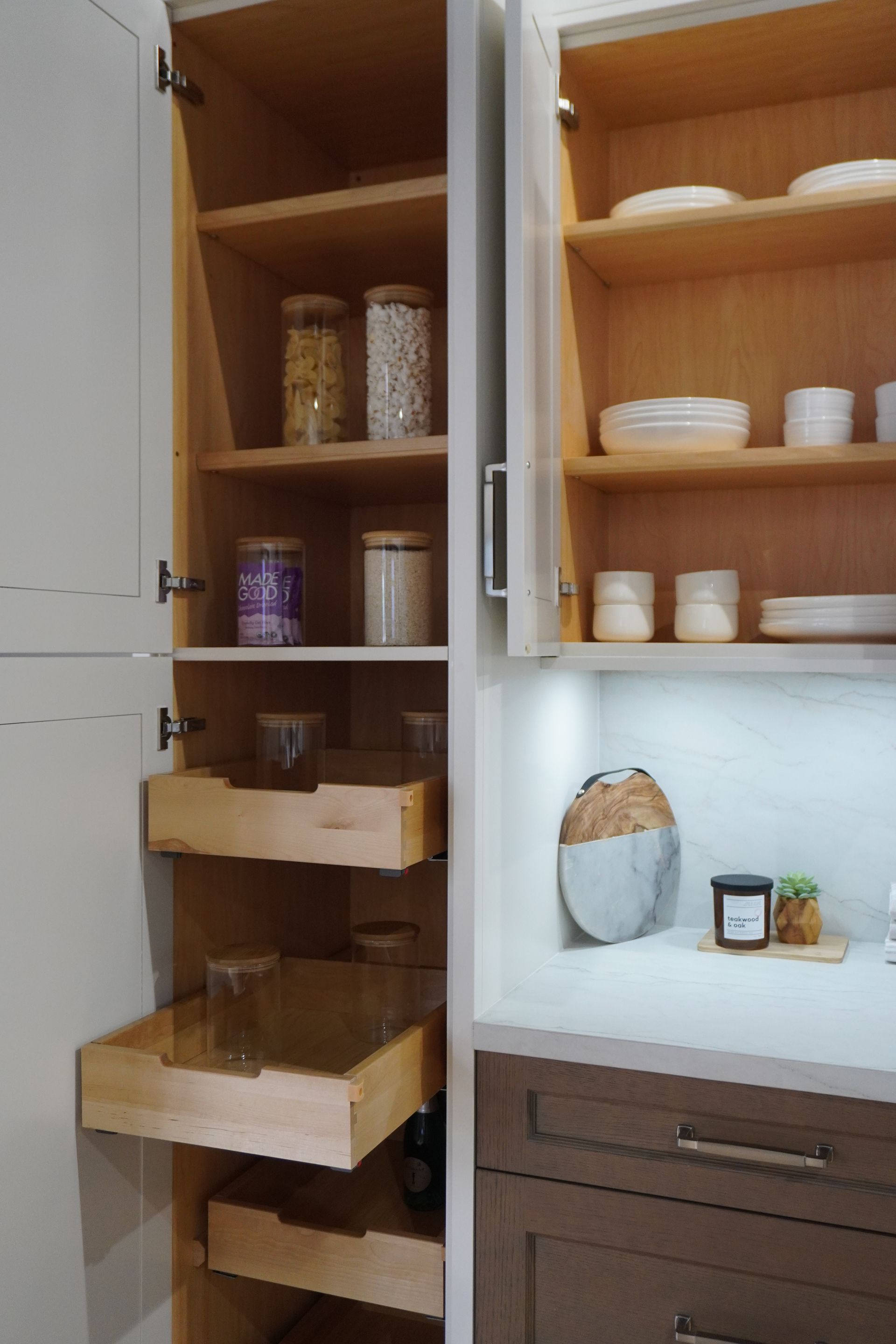 Open kitchen cabinet with wooden shelves, jars, bowls, cups, and woven storage baskets