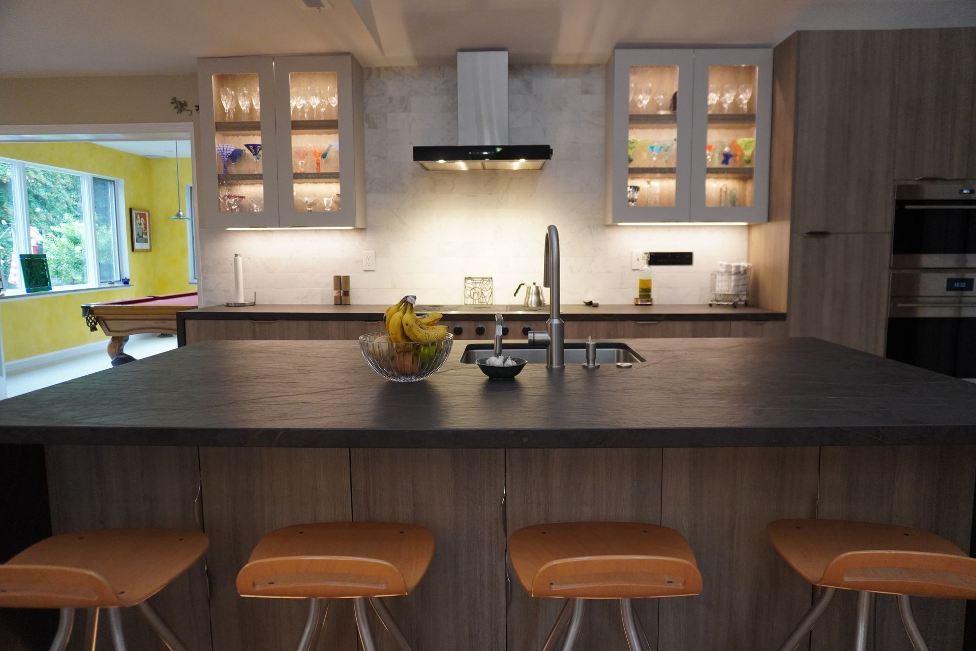 Modern kitchen with a large island, brown stools, and white cabinets, lit by under-cabinet lights.