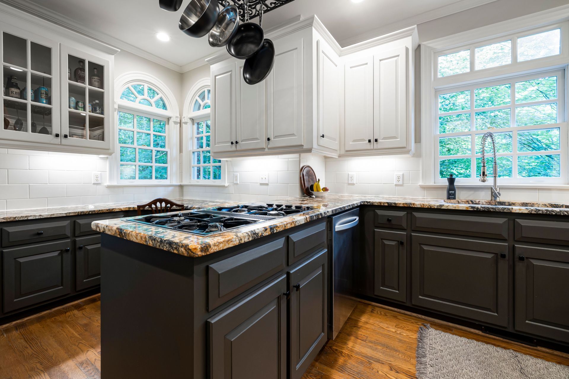 Modern kitchen with dark cabinets, white countertops, large windows, and a central island with pendant lights