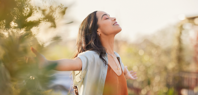 Person with arms outstretched, smiling in a sunlit field with soft bokeh background.