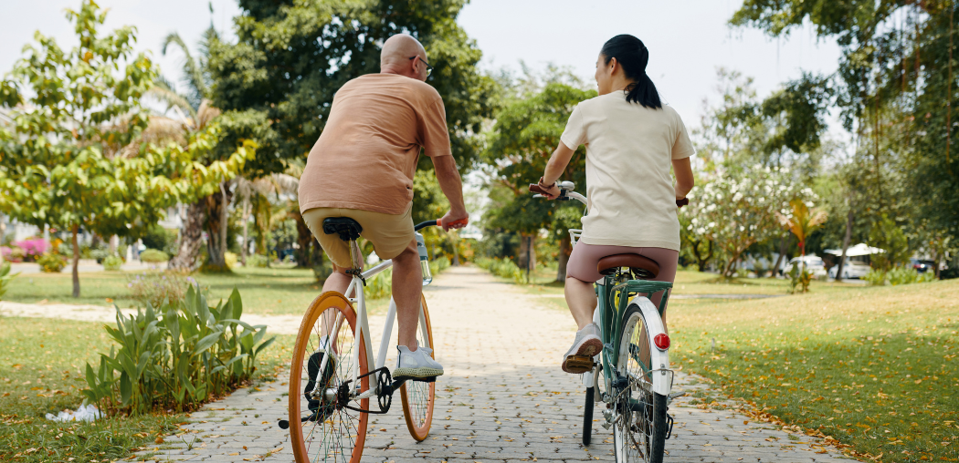 Two people riding bicycles on a tree-lined path in a park