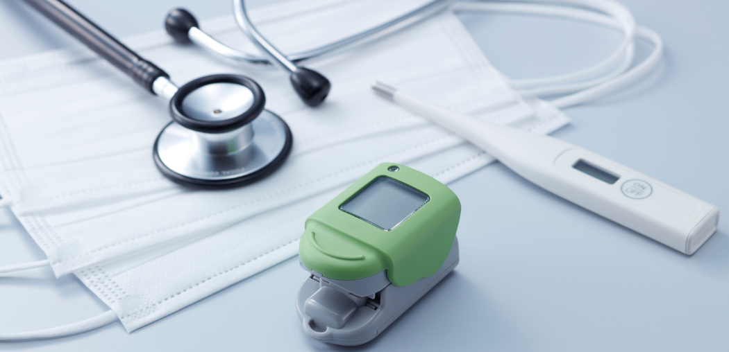 Stethoscope and papers beside a green pulse oximeter on a white medical desk