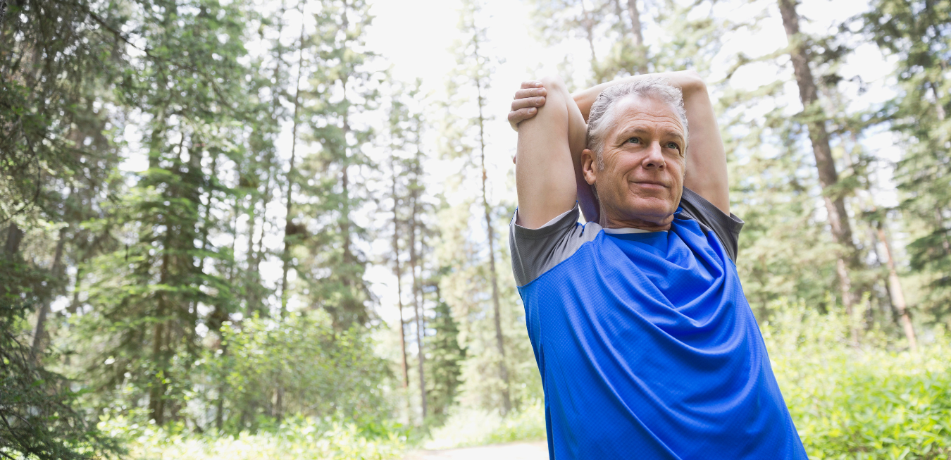 Man in blue shirt stretching outdoors in a sunny wooded area