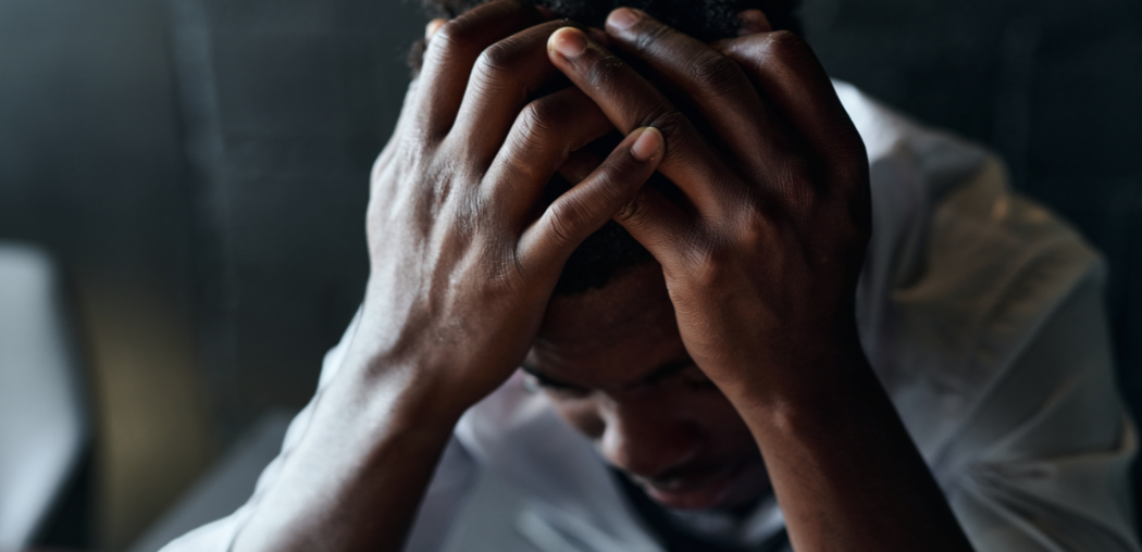 Person with head in hands, appearing stressed or distressed in a dimly lit room