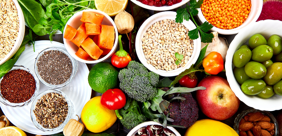 Assorted fresh fruits, vegetables, nuts, and grains arranged in bowls on a white surface