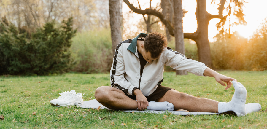 Person stretching on a yoga mat in a sunny park, with towels and trees in the background