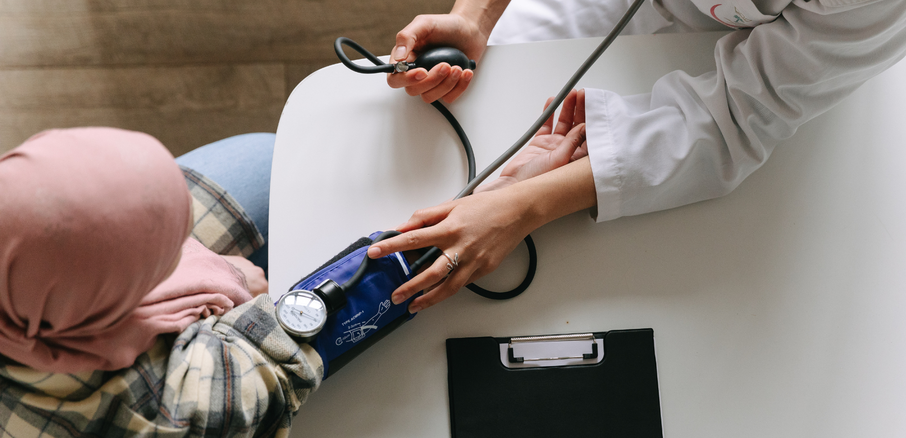 Clinician taking a blood pressure reading from a seated patient at a desk