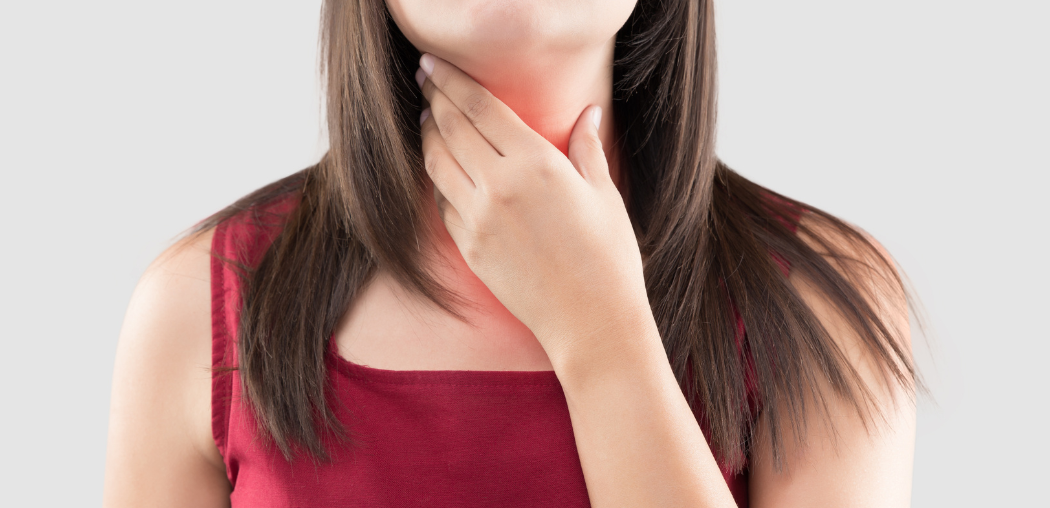 Woman holding her throat with a pained expression, wearing a red top on a light background
