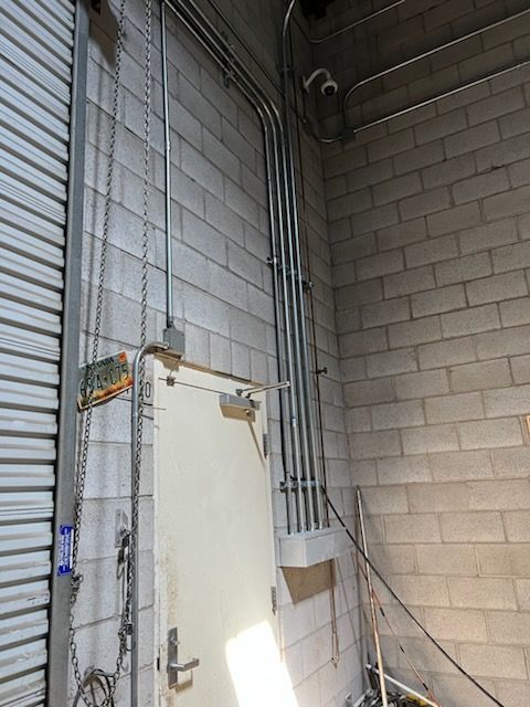 Metal conduit pipes running up a gray cinder block wall next to a white door.