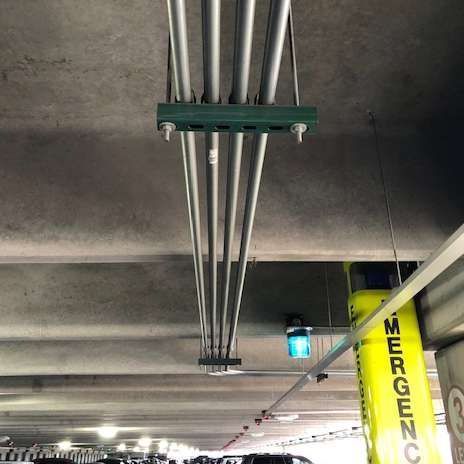 Overhead view of electrical conduit pipes suspended from a concrete ceiling in a parking garage.