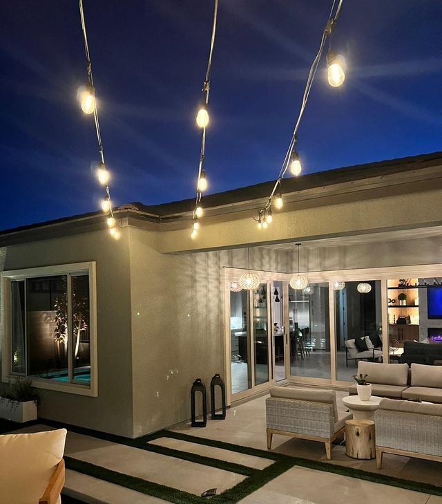 Patio with string lights. Cream-colored home with outdoor seating, green grass, and dark blue evening sky.
