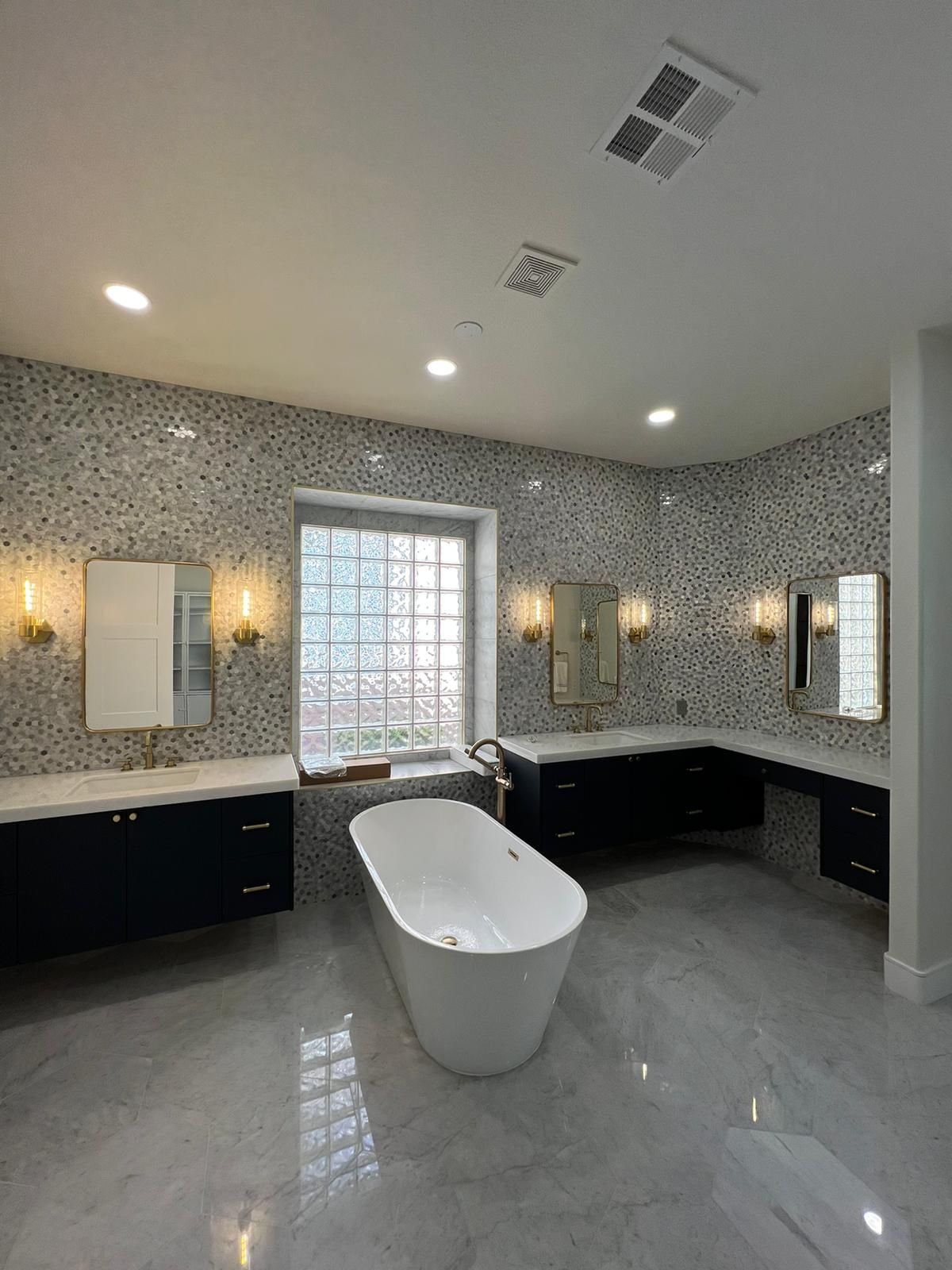Spacious modern bathroom with freestanding tub, dark cabinets, mosaic tile walls, and large window.