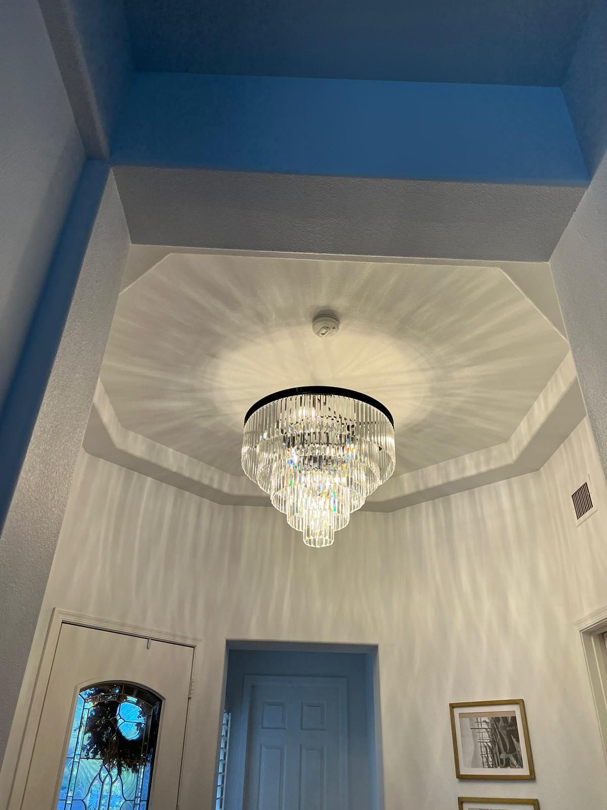 Crystal chandelier hangs in a white octagon ceiling. Blue door and walls.