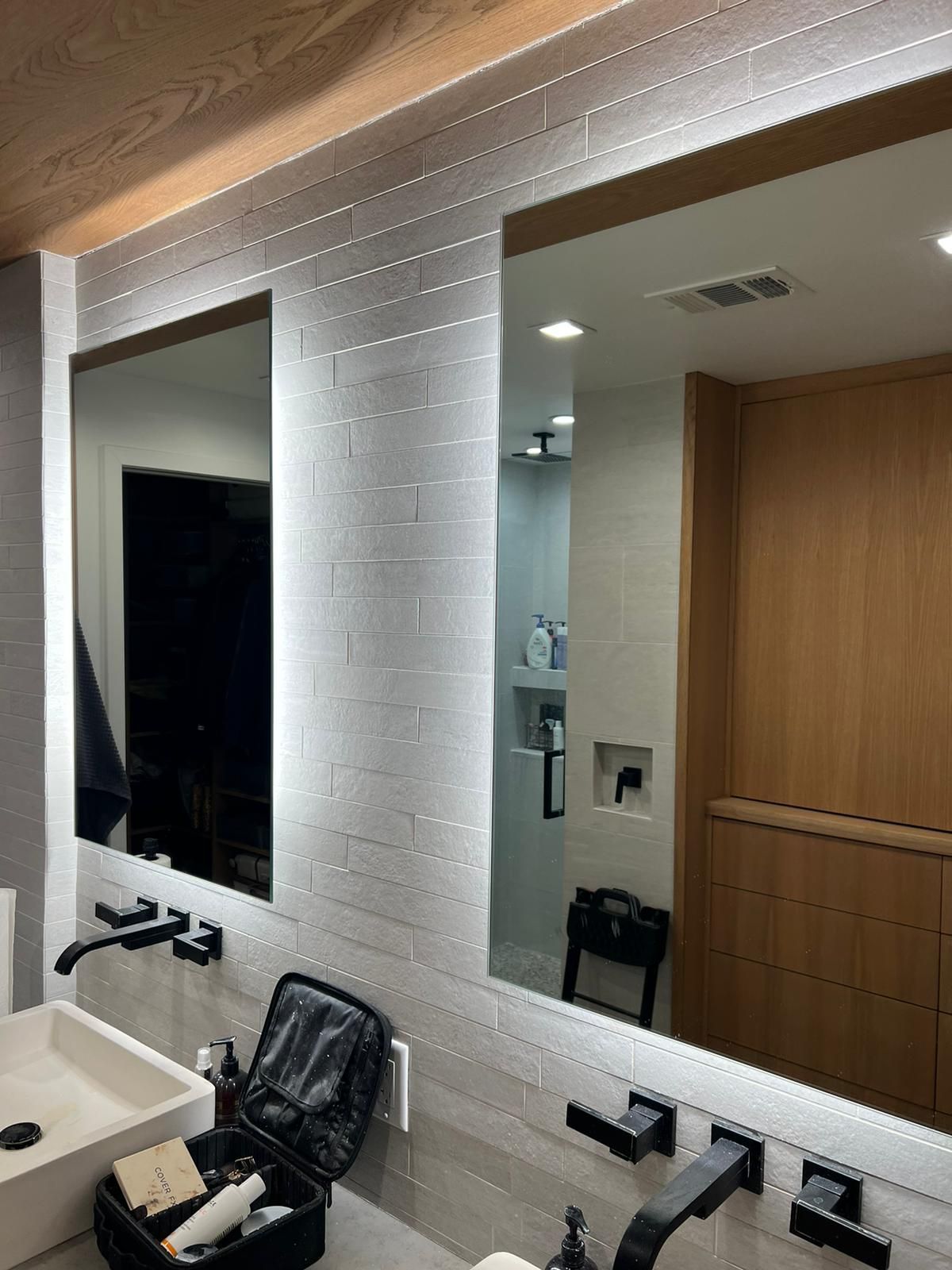 Bathroom with two mirrors, recessed lighting, white brick wall, and black faucets.
