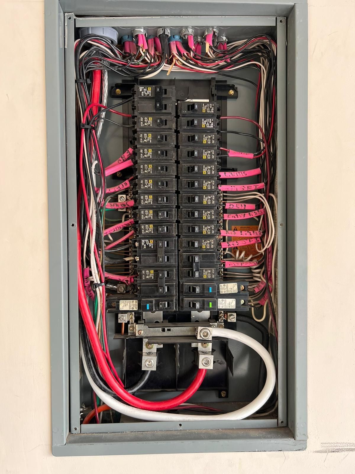 Open electrical panel with black breakers, colored wires, and silver bus bars.