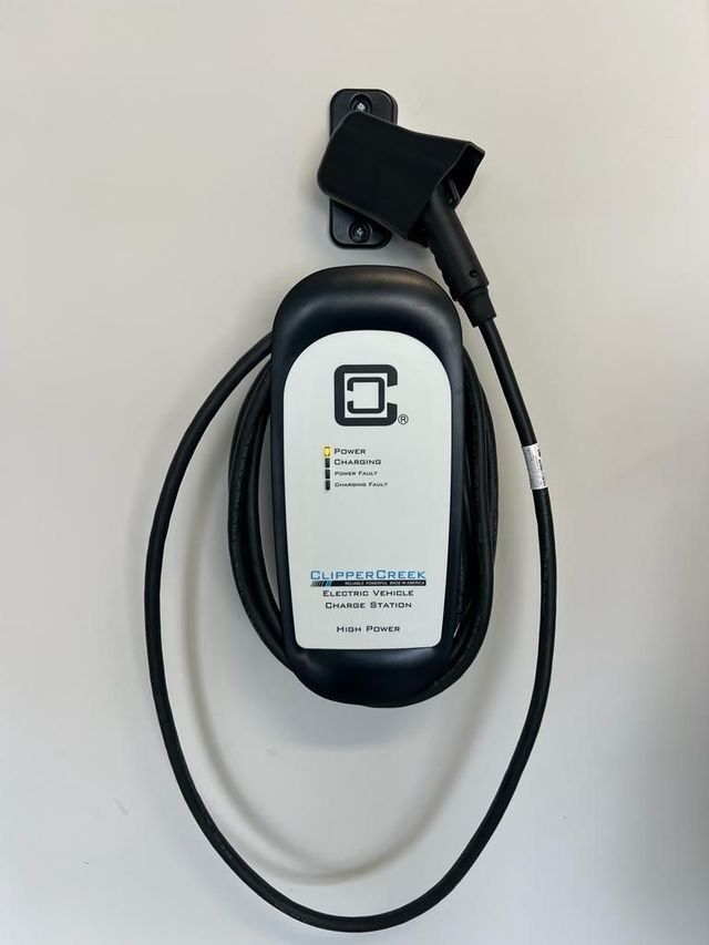 EV charger mounted on a wall; black and white unit with a black cable and a holster for the charging nozzle.