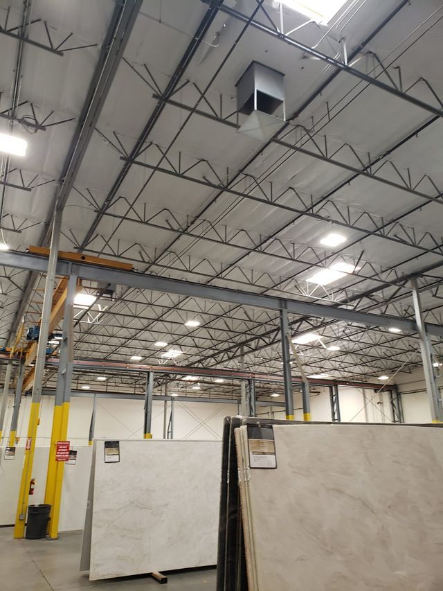 Warehouse interior with high ceiling, metal beams, skylights. Large slabs of stone are visible.