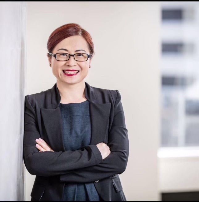 A woman wearing glasses is leaning against a wall with her arms crossed