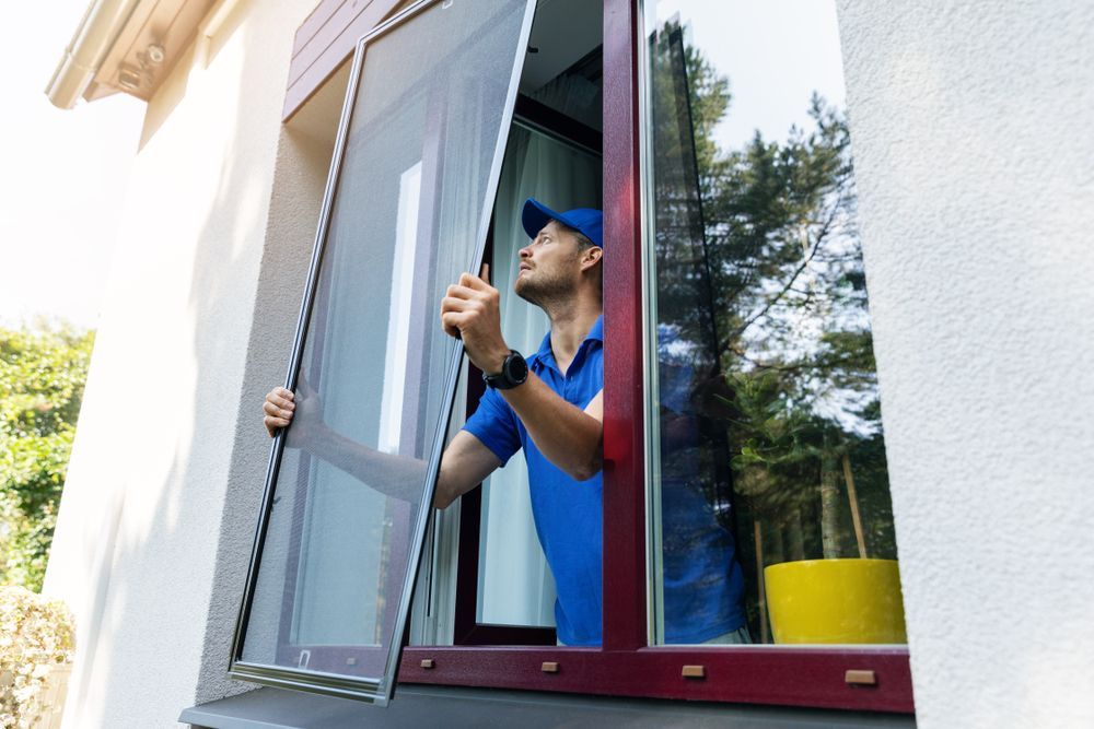A Man is Installing a Mosquito Screen on a Window — Whitsunday Architectural Windows & Doors in Proserpine, QLD