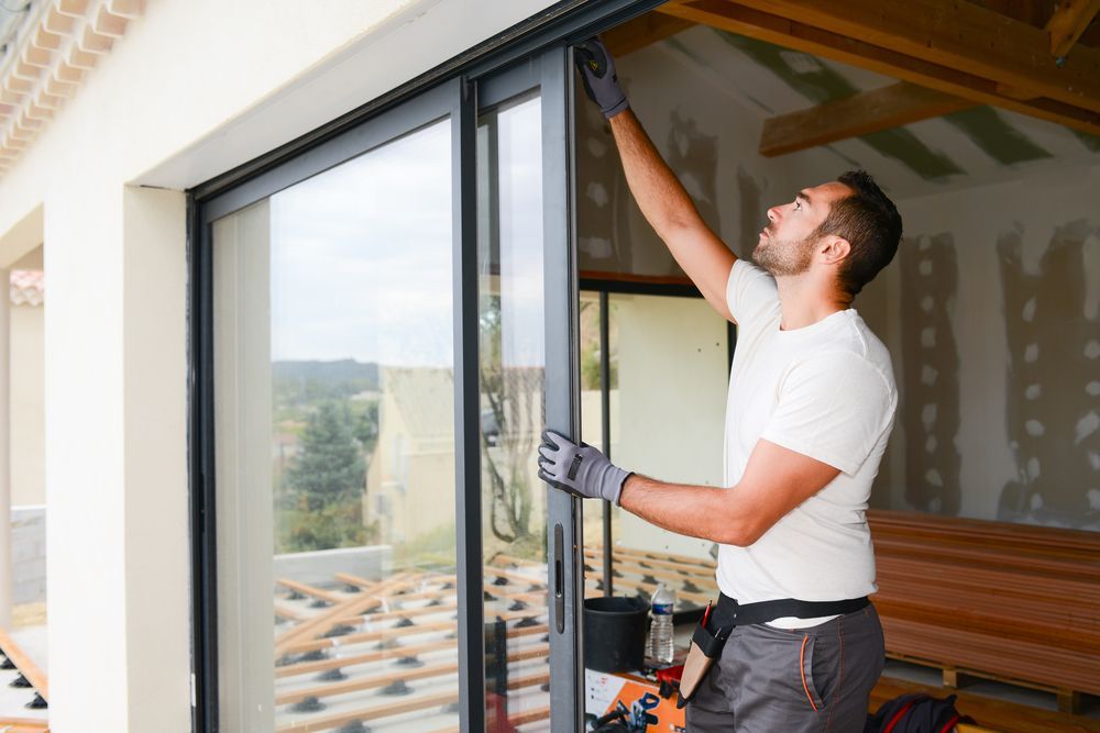 A Man is Installing a Sliding Glass Door in a House — Whitsunday Architectural Windows & Doors in Airlie Beach, QLD