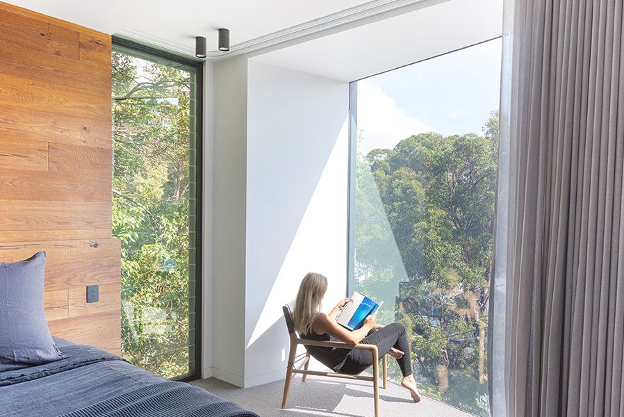 A Woman is Sitting in a Chair in Front of a Window Reading a Book — Whitsunday Architectural Windows & Doors in Proserpine, QLD