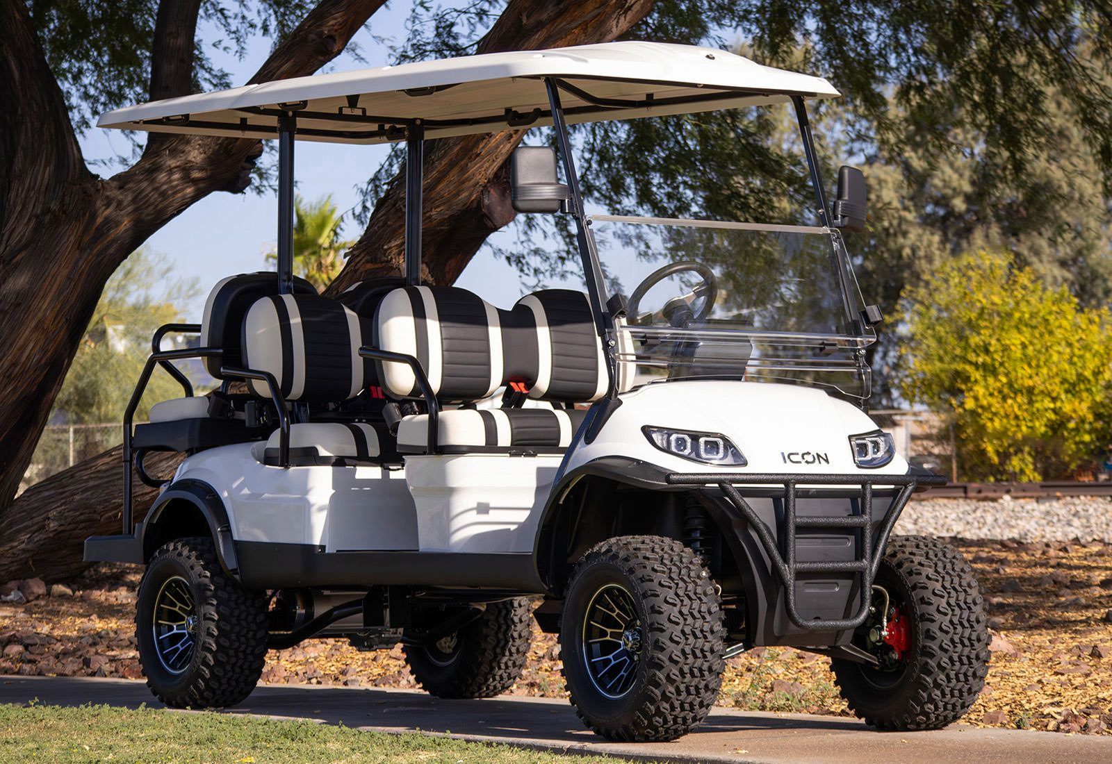 White ICON golf cart with black accents and large off-road tires, parked outdoors.