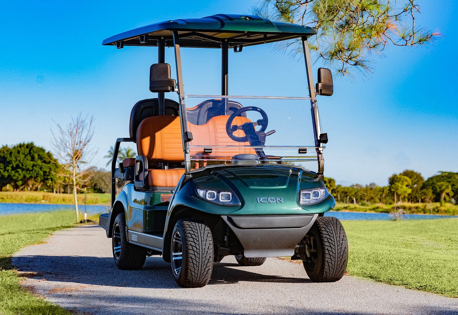 Green golf cart with tan seats on a path, overlooking a lake.