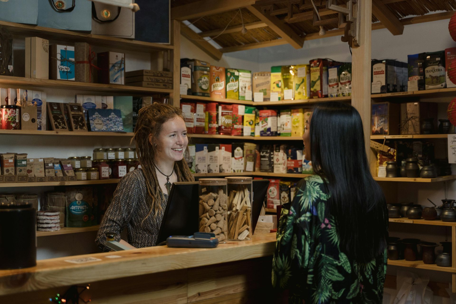 Two women are standing at a counter in a store talking to each other.