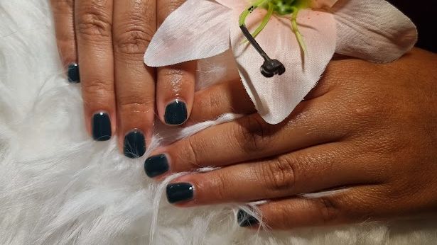 De hand van een vrouw met zwarte nagels houdt een roze bloem vast.