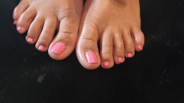 Een close-up van de voeten van een vrouw met roze nagels op een zwart oppervlak.